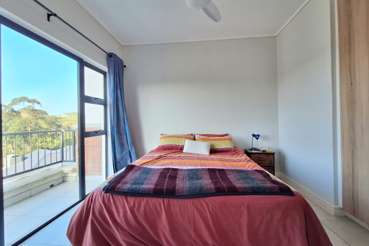 A bright bedroom featuring tiled flooring, a ceiling fan, and a built-in wardrobe, with direct access to a private balcony through sliding glass doors.