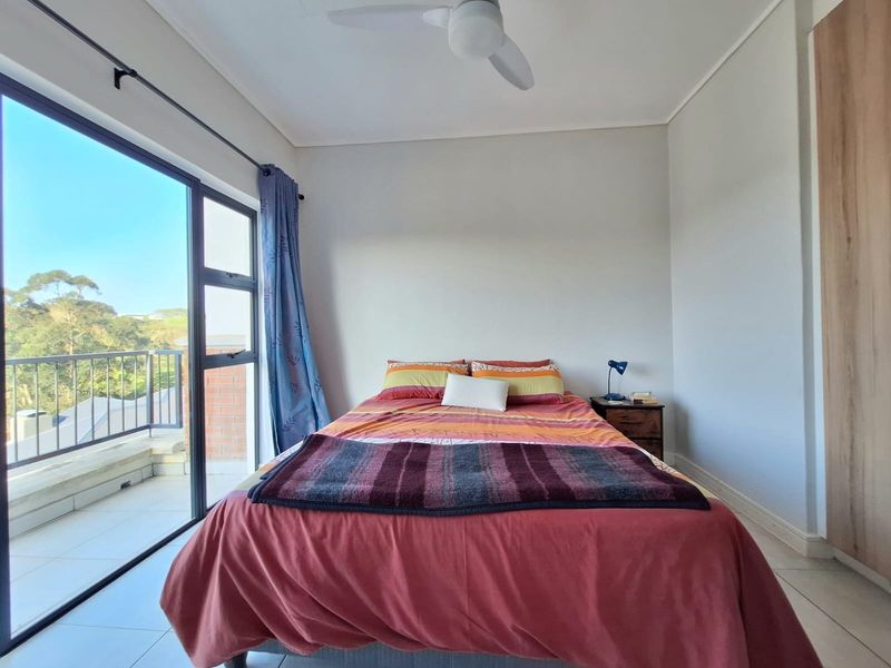 A bright bedroom featuring tiled flooring, a ceiling fan, and a built-in wardrobe, with direct access to a private balcony through sliding glass doors.
