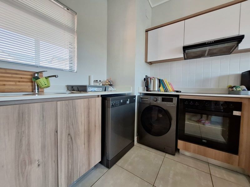 Modern kitchen featuring wood-look cabinetry, stone-style countertops, built-in oven with extractor fan, and tiled flooring, offering a functional and contemporary cooking space.