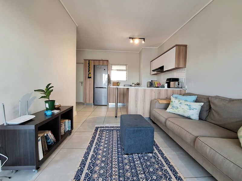 An open-plan living area featuring a modern kitchen with wood-finish cabinetry, a breakfast bar, and neutral tiled flooring throughout.
