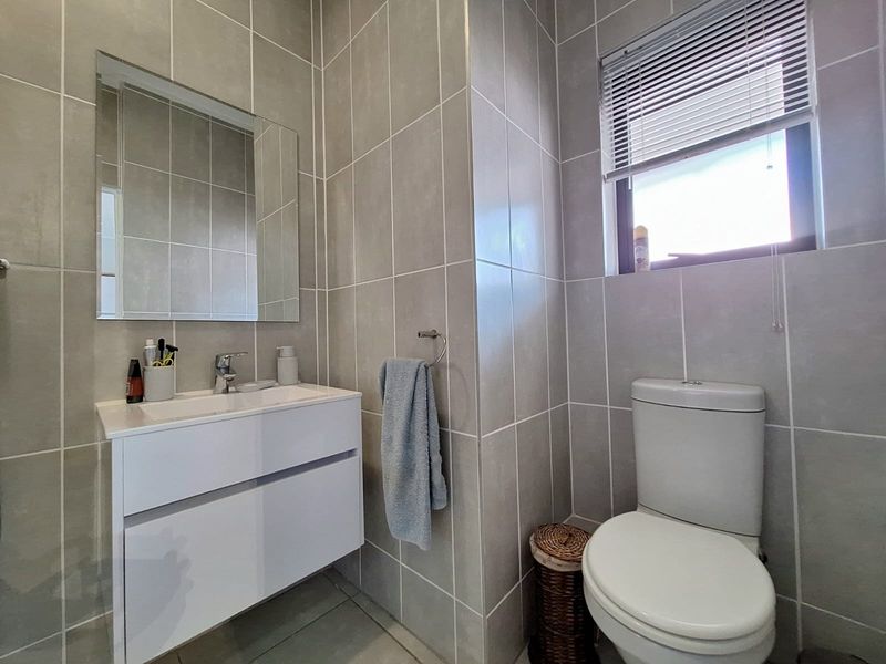 Modern bathroom featuring floor-to-ceiling grey tiling, a sleek wall-mounted vanity with basin, and a dual-flush toilet.