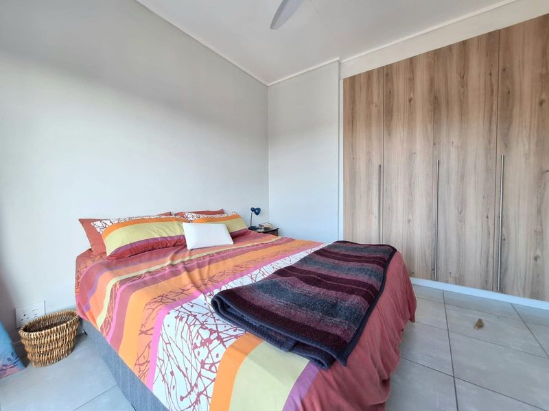 A well-maintained bedroom featuring neutral tiled flooring, a ceiling fan, and modern wood-finish built-in cupboards providing ample storage space.