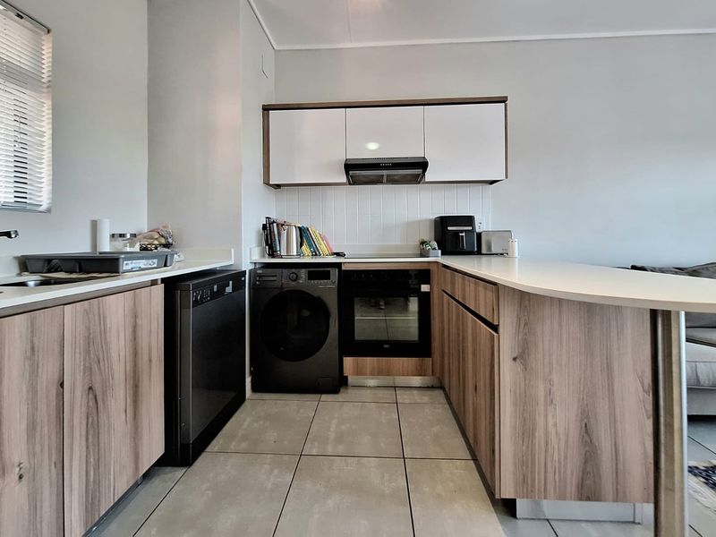 Modern kitchen featuring wood-finish cabinetry, integrated oven, extractor fan, and a breakfast bar counter, complemented by neutral tiled flooring and backsplash.
