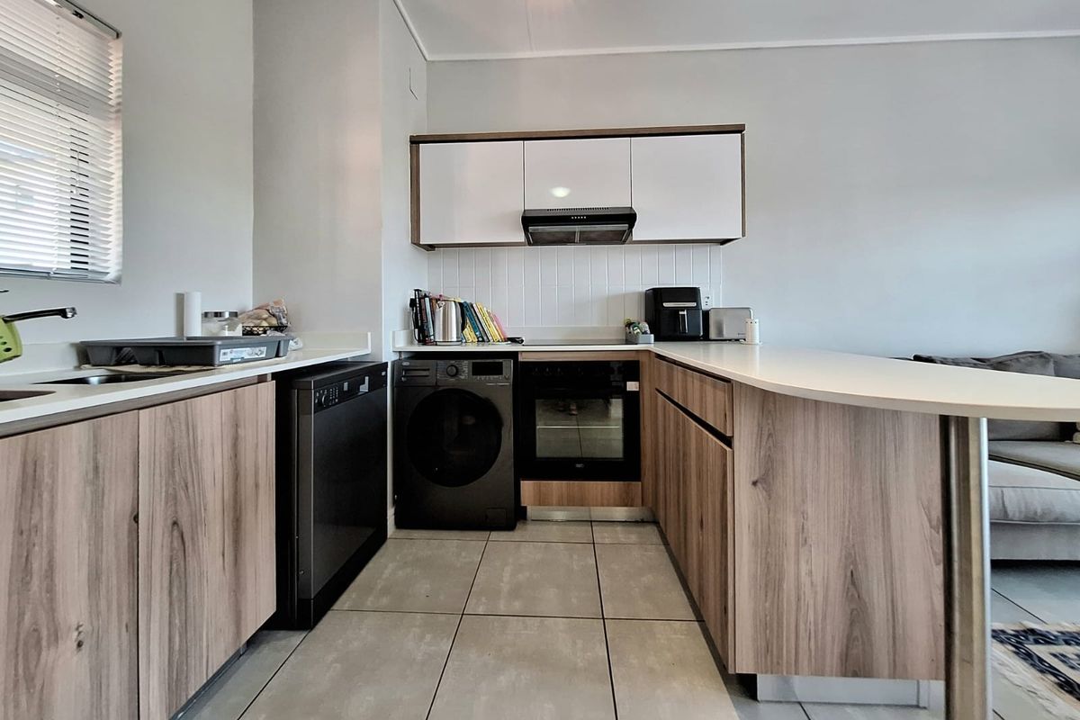 Modern kitchen featuring wood-finish cabinetry, integrated oven, extractor fan, and a breakfast bar counter, complemented by neutral tiled flooring and backsplash.