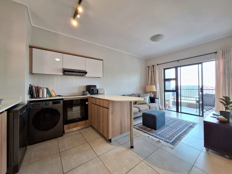 Open-plan living area featuring a modern kitchen with built-in cabinetry, oven, and extractor fan, leading to a balcony through sliding glass doors.
