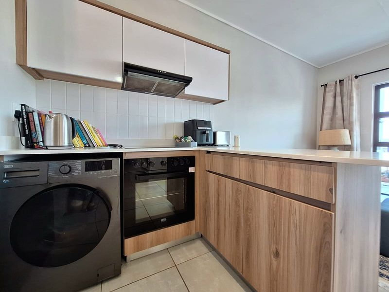Modern kitchen featuring wood-finish cabinetry, white tiled backsplash, built-in oven, extractor fan, and integrated laundry appliance space.