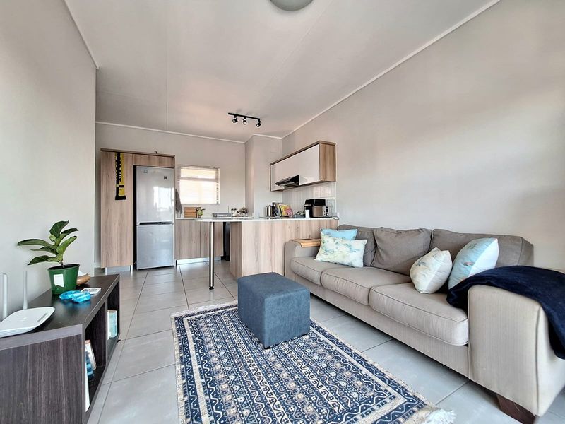 An open-plan living area featuring a modern kitchen with built-in cabinetry, a breakfast counter, and neutral tiled flooring throughout.