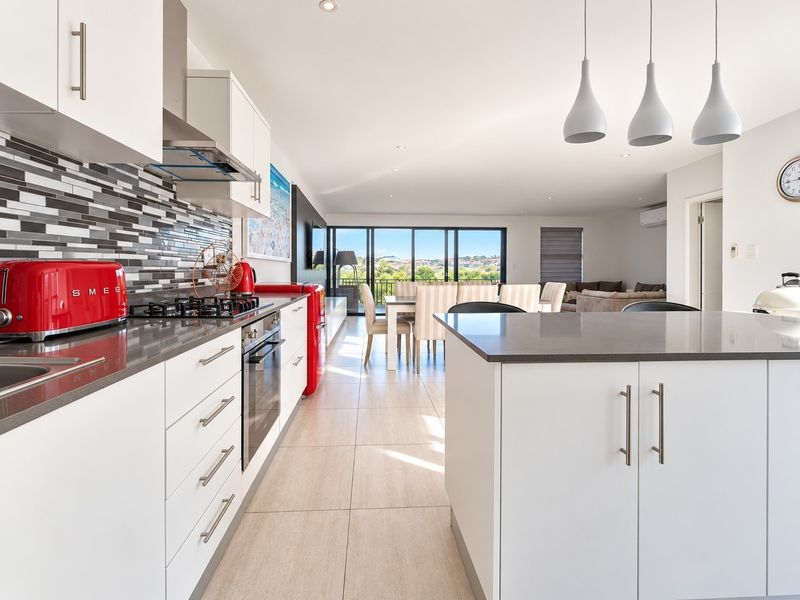 Modern open-plan kitchen and living area featuring stone countertops, gas cooktop, sleek cabinetry, and large sliding doors leading to an outdoor view.