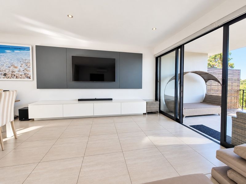 Modern living room featuring a sleek built-in media console, large format floor tiles, and expansive sliding glass doors opening to a patio area.