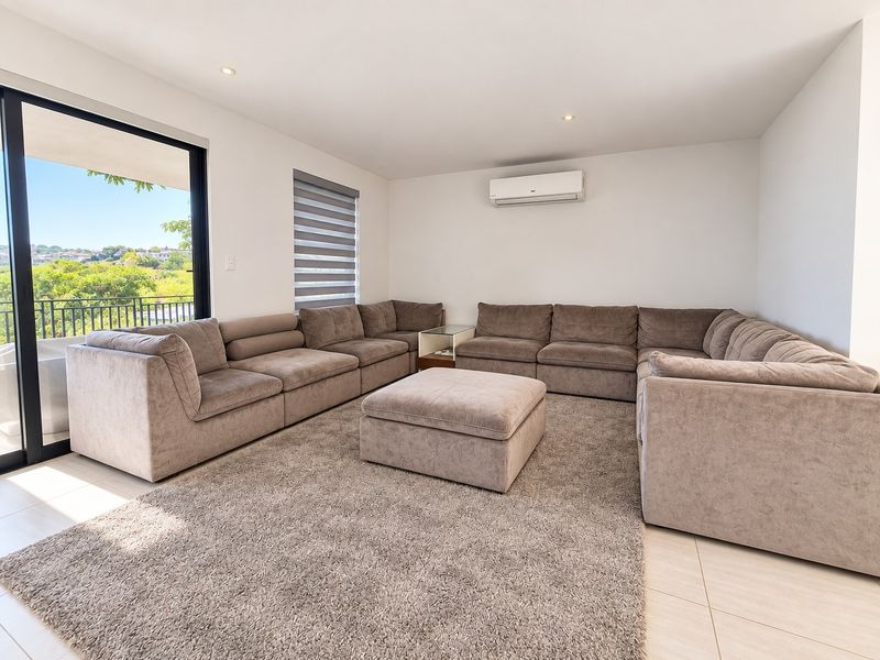 A bright and modern living room featuring tiled floors, recessed lighting, a wall-mounted air conditioner, and large sliding doors leading to an outdoor area.