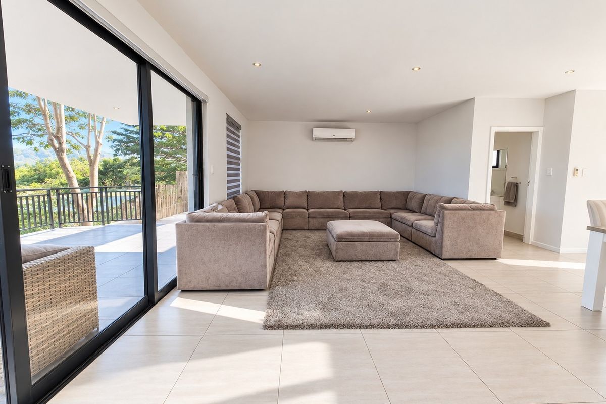 Spacious, light-filled living room featuring large sliding glass doors that open onto a patio, tiled flooring, and a wall-mounted air conditioning unit.