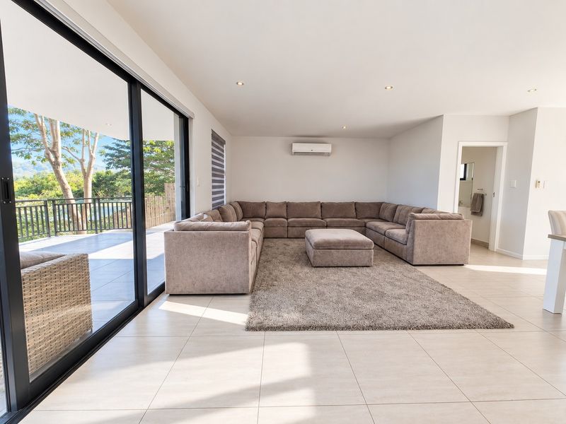 Spacious, light-filled living room featuring large sliding glass doors that open onto a patio, tiled flooring, and a wall-mounted air conditioning unit.
