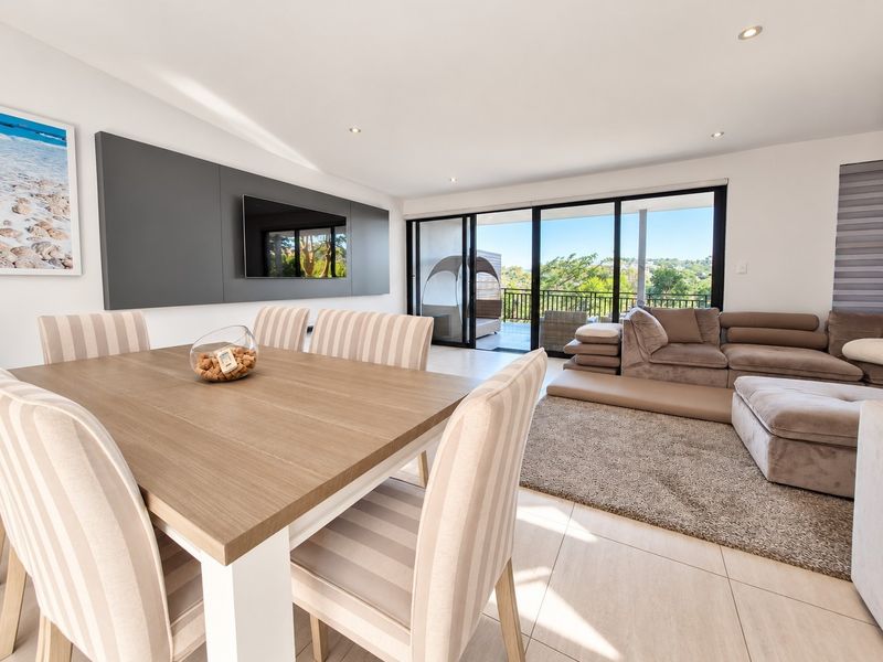 Bright open-plan living and dining area featuring modern tiled floors, recessed lighting, and large sliding glass doors leading to an outdoor balcony.