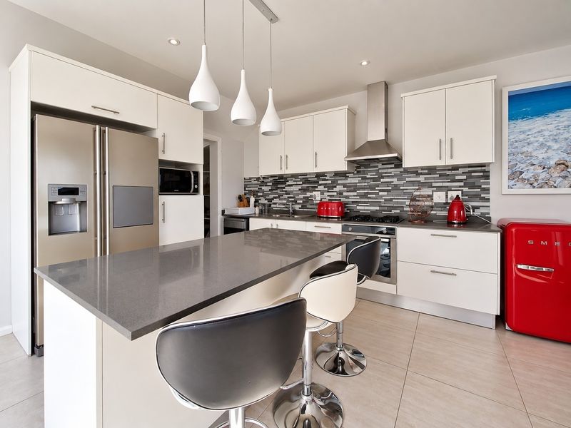 Modern kitchen featuring a central island with stone countertops, mosaic tile backsplash, stainless steel appliances, and ample built-in cabinetry.