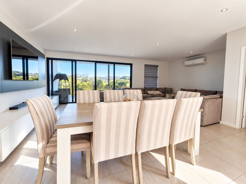 Spacious open-plan living and dining area featuring tiled floors, recessed lighting, air conditioning, and large sliding doors leading to an outdoor balcony with views.