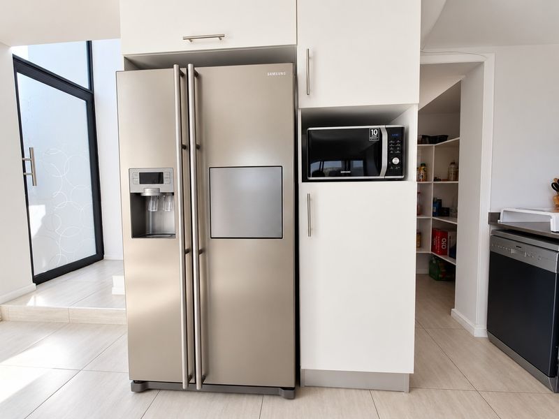 Modern kitchen area featuring built-in cabinetry, integrated microwave, dishwasher, and a convenient walk-in pantry with tiled flooring throughout.