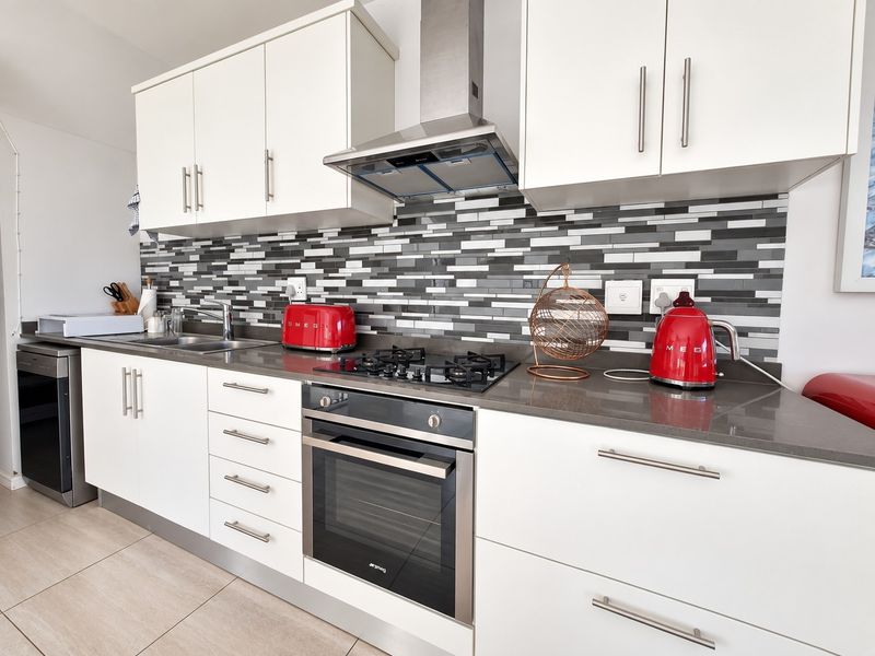 Modern kitchen featuring white cabinetry, stone countertops, a gas hob with extractor fan, and a contemporary mosaic tile backsplash.