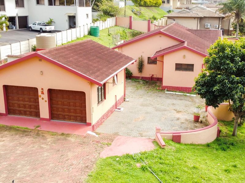 Aerial view of a residential property featuring a double garage, paved driveway, and perimeter walling on a sloped plot.