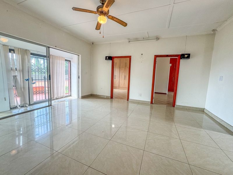 Spacious living area featuring large sliding glass doors, tiled flooring, a ceiling fan, and direct access to adjacent rooms with built-in storage.