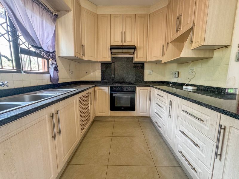 A functional kitchen featuring light wood-finish cabinetry, granite countertops, a built-in oven with hob, and tiled flooring.