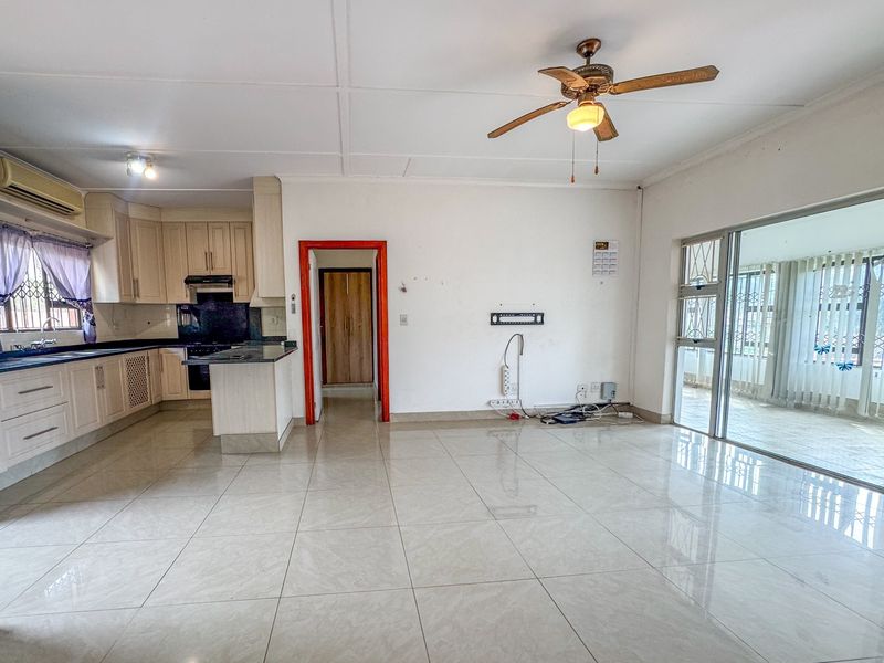 Spacious open-plan living and kitchen area featuring tiled floors, built-in cabinetry, ceiling fan, and direct access to an enclosed patio through sliding glass doors.