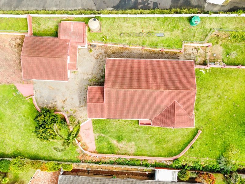 Aerial view of the property showing the main house, detached structure, paved driveway, and surrounding garden area with boundary walls.