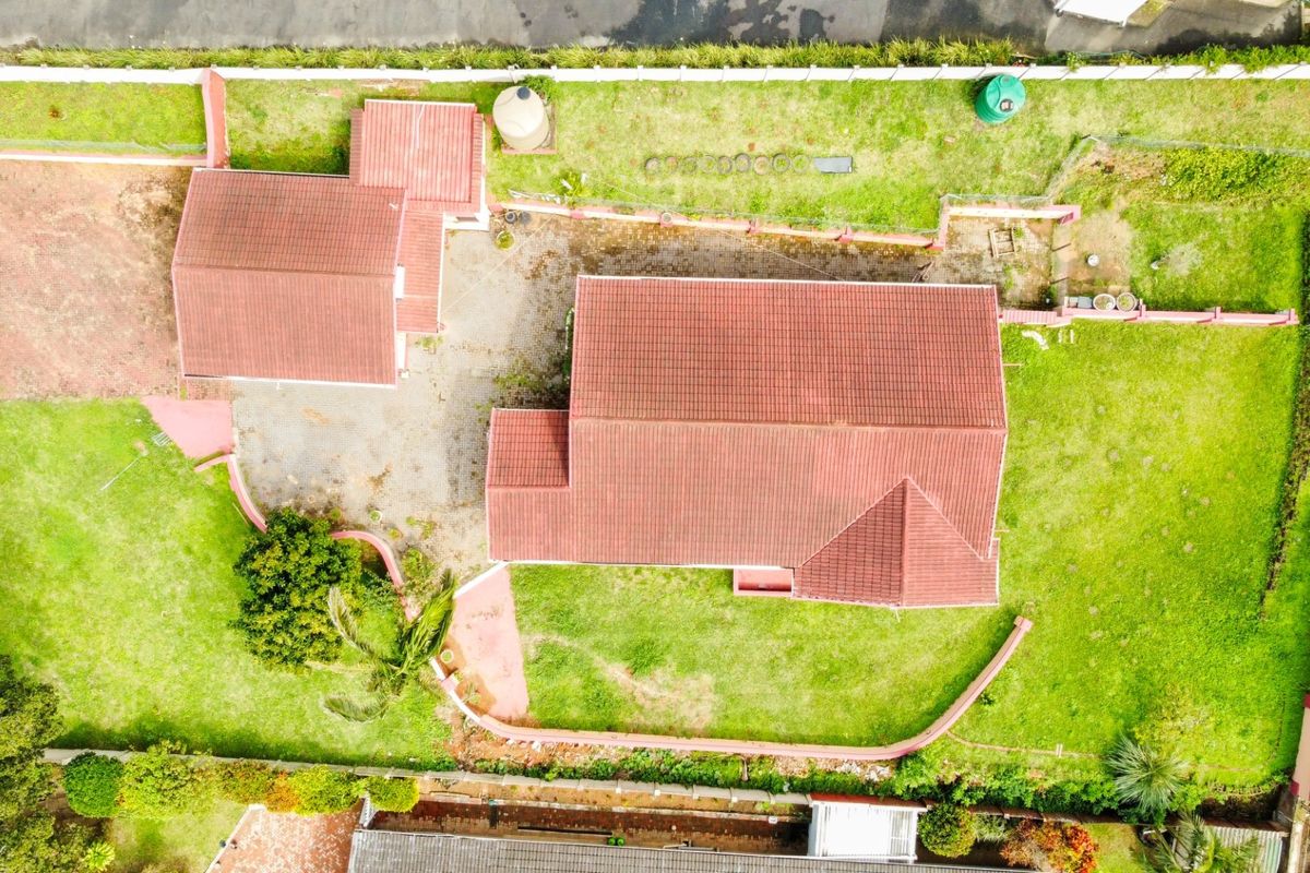 Aerial view of the property showing the main house, detached structure, paved driveway, and surrounding garden area with boundary walls.