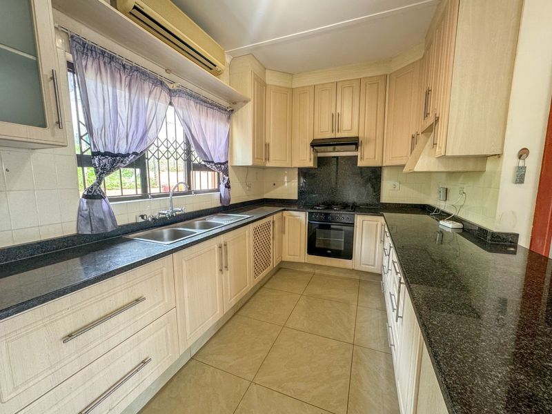 Functional kitchen featuring granite countertops, built-in oven, gas hob, extractor fan, and ample cabinetry, providing a practical workspace for daily cooking.
