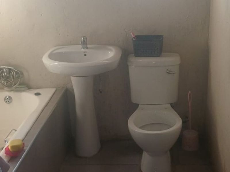 A functional bathroom featuring a pedestal basin, toilet, and built-in bathtub with tiled flooring and security-barred windows.