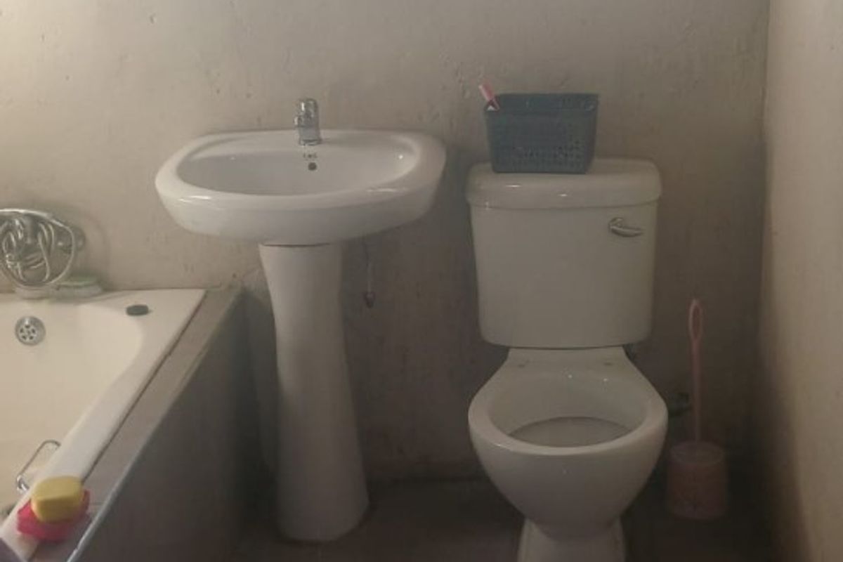 A functional bathroom featuring a pedestal basin, toilet, and built-in bathtub with tiled flooring and security-barred windows.