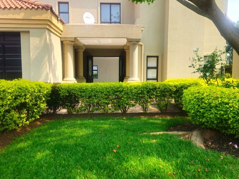 Front view of a residential property featuring a covered entrance with columns, a garage, and a well-maintained garden.