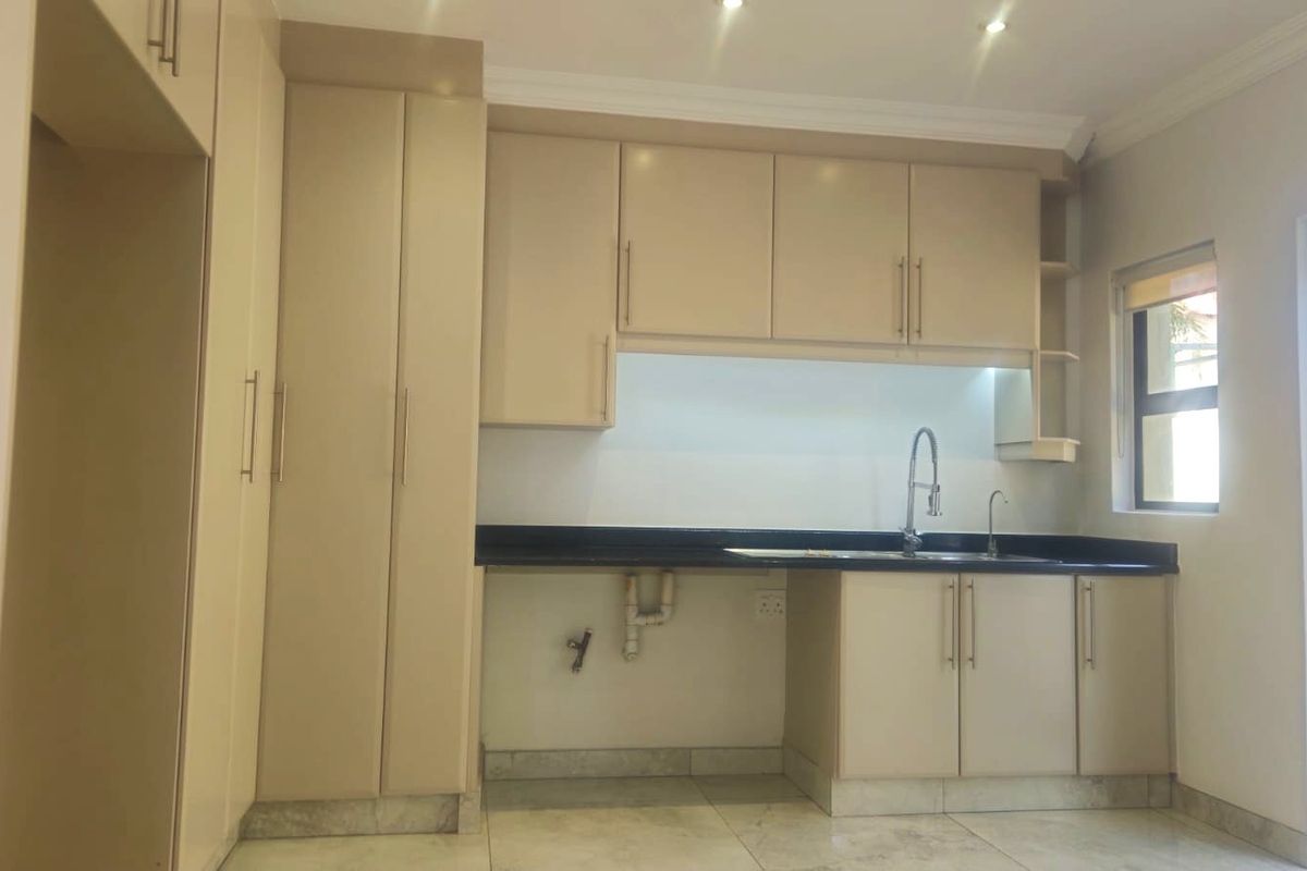 A clean, empty kitchen featuring neutral built-in cabinetry, dark granite countertops, and tiled flooring, ready for appliance installation.
