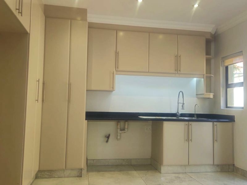 A clean, empty kitchen featuring neutral built-in cabinetry, dark granite countertops, and tiled flooring, ready for appliance installation.