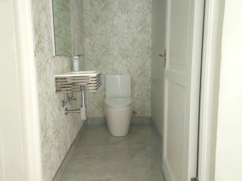 A compact guest bathroom featuring a wall-mounted basin, modern toilet, and decorative wallpaper finish.