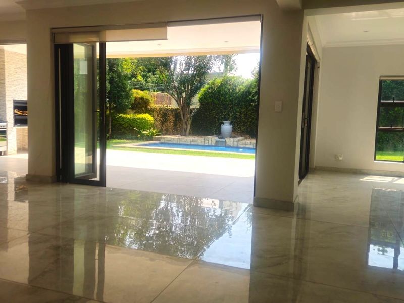 Spacious open-plan living area featuring large format polished tiles, seamless indoor-outdoor flow through stacking doors, and a view of the private garden and pool.