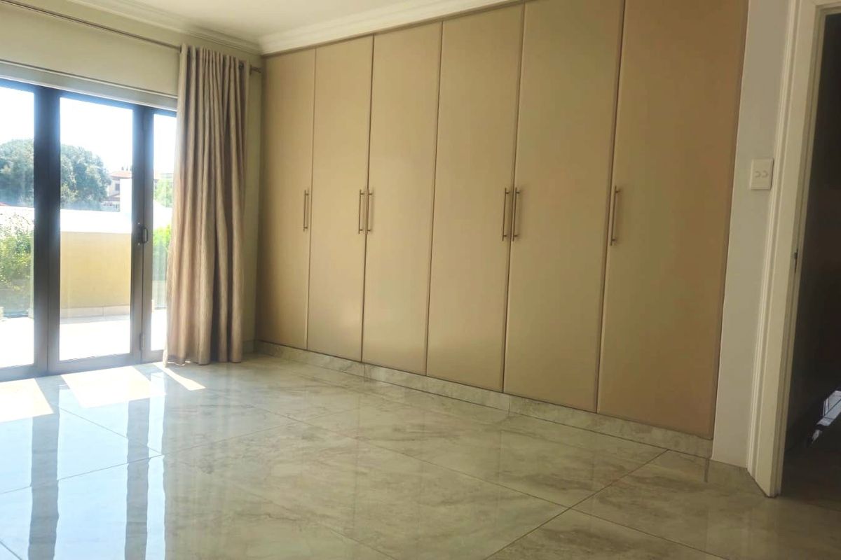 Spacious bedroom featuring large built-in cupboards, polished tiled flooring, and a sliding glass door providing access to an outdoor area.
