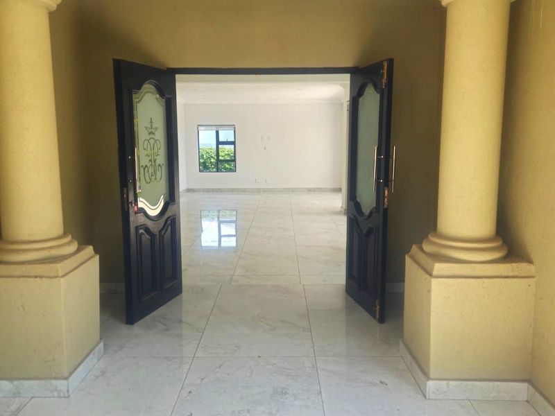 Spacious entrance hall featuring double doors, decorative columns, and polished porcelain floor tiles leading into an open-plan living area.