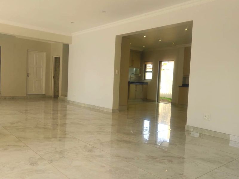 Spacious open-plan living area featuring polished porcelain floor tiles, recessed lighting, and a seamless transition to the kitchen and outdoor patio area.