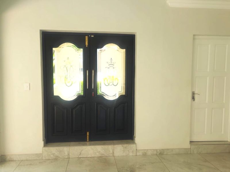 A bright entrance hall featuring a dark double front door with decorative glass inserts, tiled flooring, and a secondary internal panel door.
