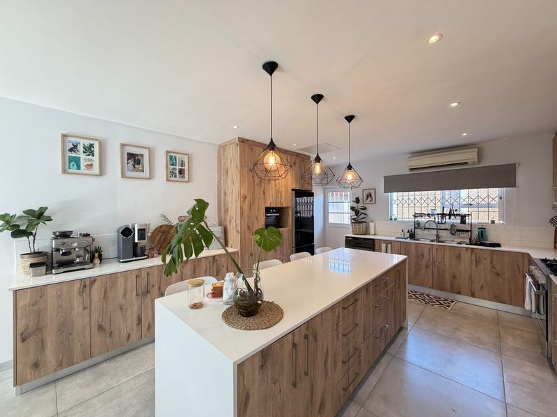 Modern kitchen featuring wood-look cabinetry, a large central island with quartz countertops, integrated appliances, and stylish pendant lighting.
