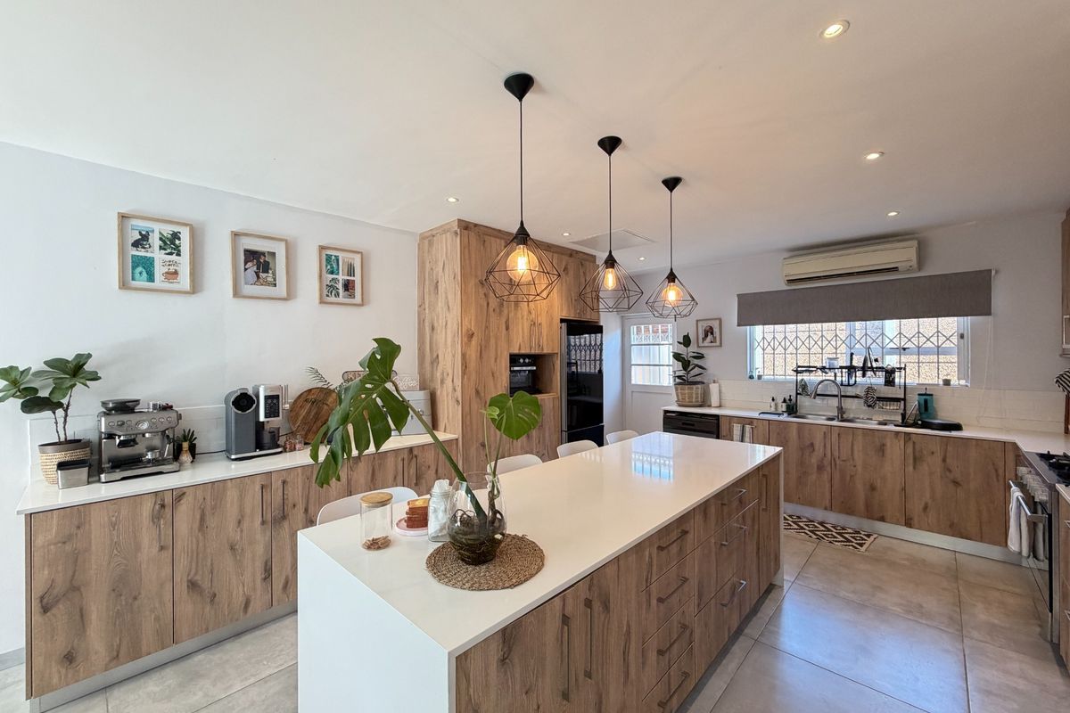 Modern kitchen featuring wood-look cabinetry, a large central island with quartz countertops, integrated appliances, and stylish pendant lighting.