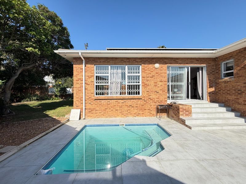 Rear exterior view featuring a swimming pool, tiled patio area, brick facade, and sliding glass door access to the home.