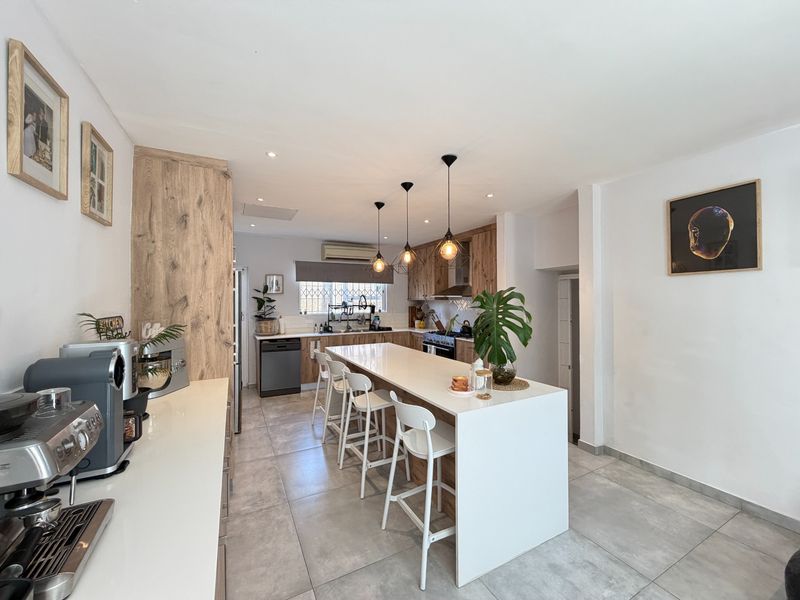 Modern kitchen featuring a central island with breakfast bar seating, wood-grain cabinetry, tiled flooring, and integrated appliances.
