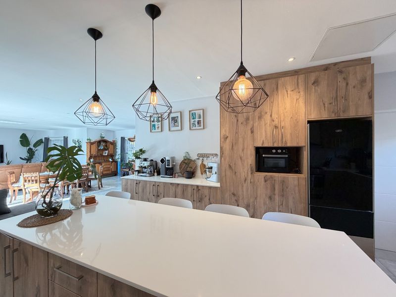 Modern open-plan kitchen featuring a large island with quartz countertops, wood-look cabinetry, and stylish pendant lighting, flowing into the adjacent dining and living area.