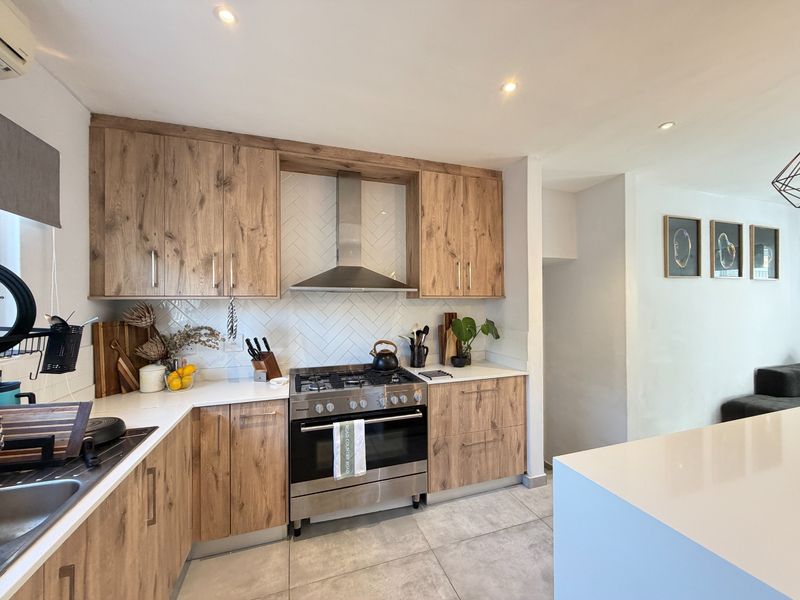 Modern kitchen featuring wood-grain cabinetry, quartz countertops, a herringbone tile backsplash, and a stainless steel gas stove with an integrated extractor fan.