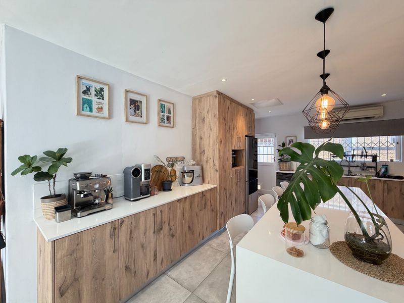 Modern kitchen featuring wood-grain cabinetry, stone countertops, a central island, and contemporary pendant lighting in an open-plan layout.