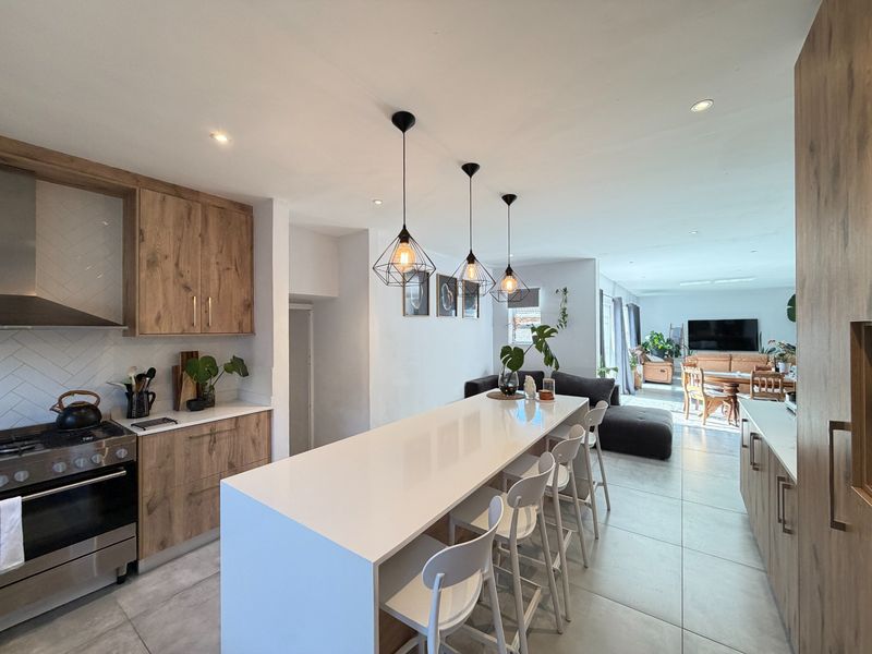 Modern open-plan kitchen featuring a large quartz island, wood-finish cabinetry, gas stove, and stylish pendant lighting, flowing into a spacious living and dining area.