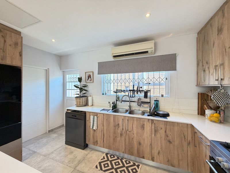 Modern kitchen featuring wood-look cabinetry, subway tile backsplash, double basin sink, and integrated air conditioning unit with tiled flooring.
