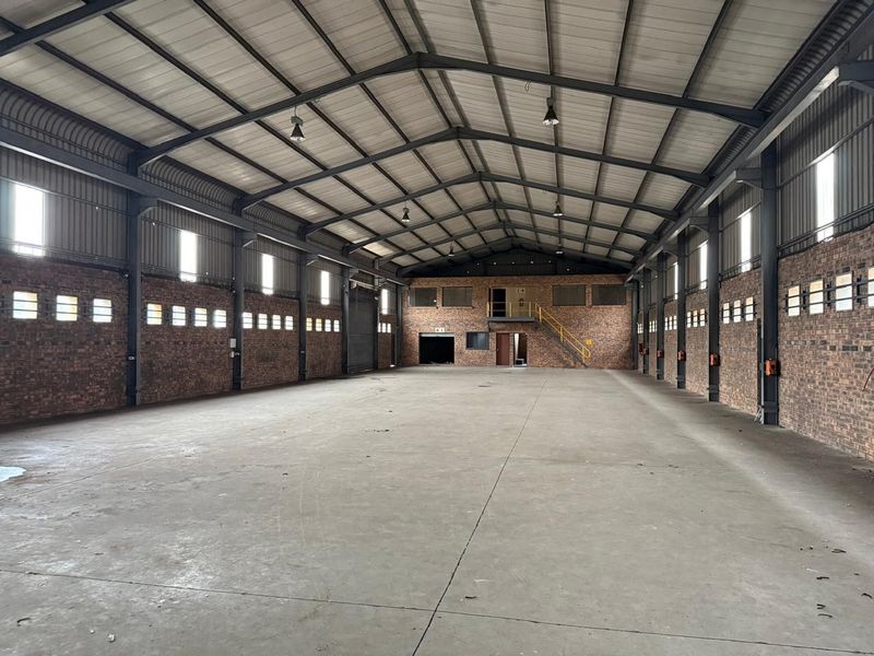 Spacious industrial warehouse featuring high ceilings with exposed steel trusses, concrete flooring, face brick walls, and a mezzanine level with staircase access.