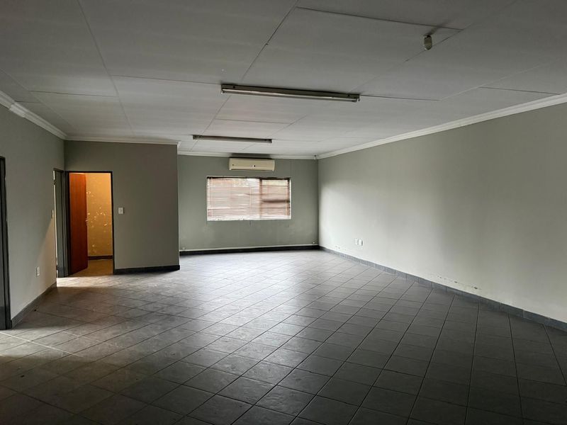 Spacious, empty industrial office area featuring tiled flooring, a split-system air conditioner, and neutral wall finishes, suitable for various commercial or administrative uses.
